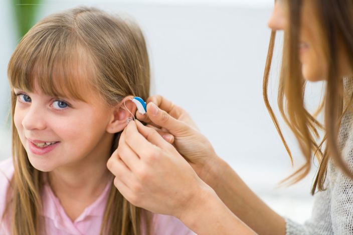 A woman putting a hearing aid on for a young girl