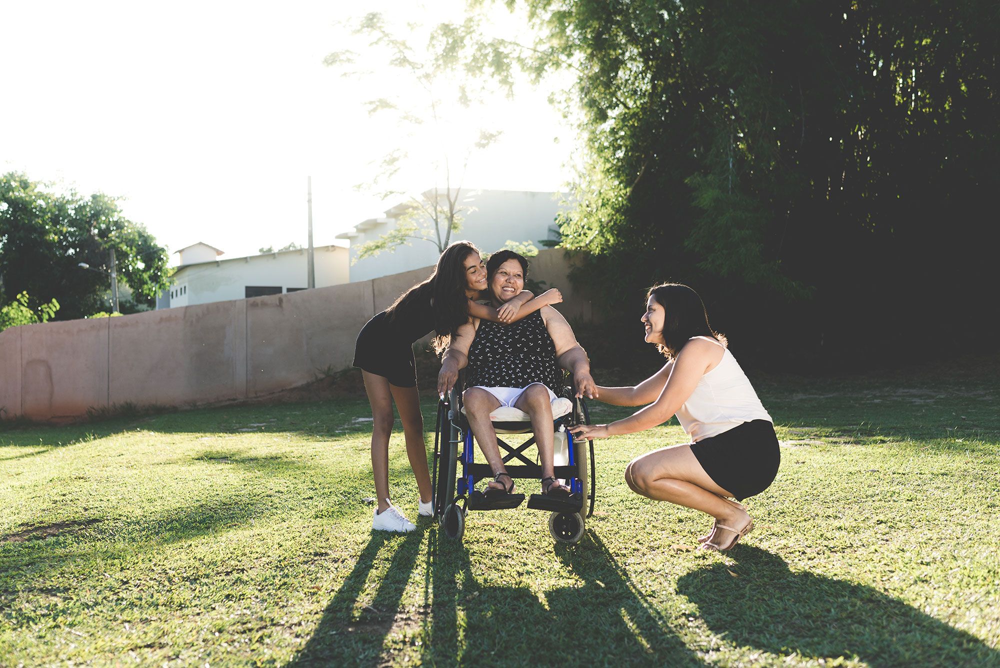 A woman in a wheelchair being hugged by a young girl and holding the hand of a young woman