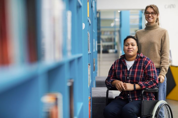 Young female PCA with glasses pushing client in a plaid shirt in a wheelchair Young female PCA with glasses pushing client in a plaid shirt in a wheelchair
